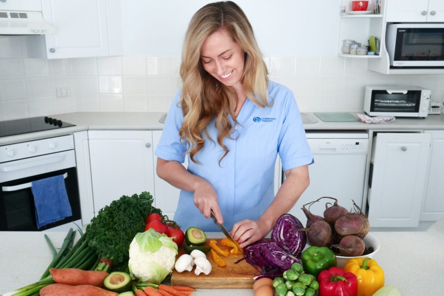 Dietitian standing behind a kitchen bench cutting vegetables on a chopping board