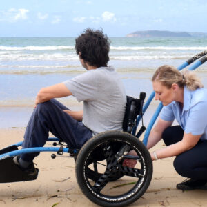 Occupational Therapist assisting a young NDIS participant on a beach wheelchair