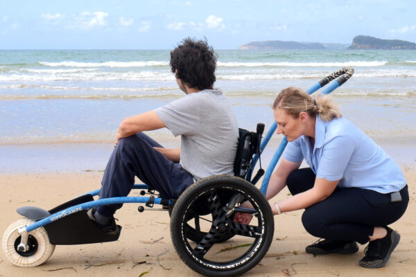 Occupational Therapist assisting a young NDIS participant on a beach wheelchair