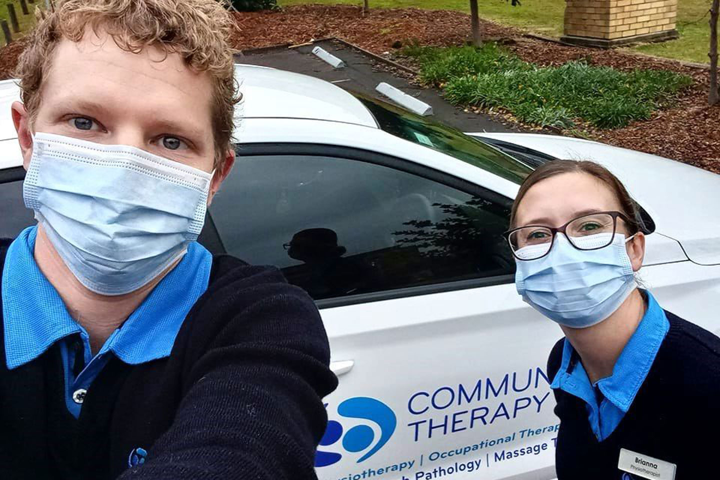 Selfie of two physiotherapists with face masks in front of a Community Therapy car
