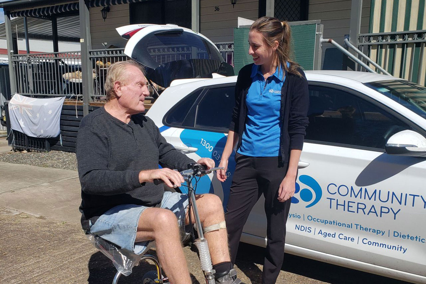 Occupational Therapist and NDIS client trialling a portable scooter with a Community Therapy branded car in the background
