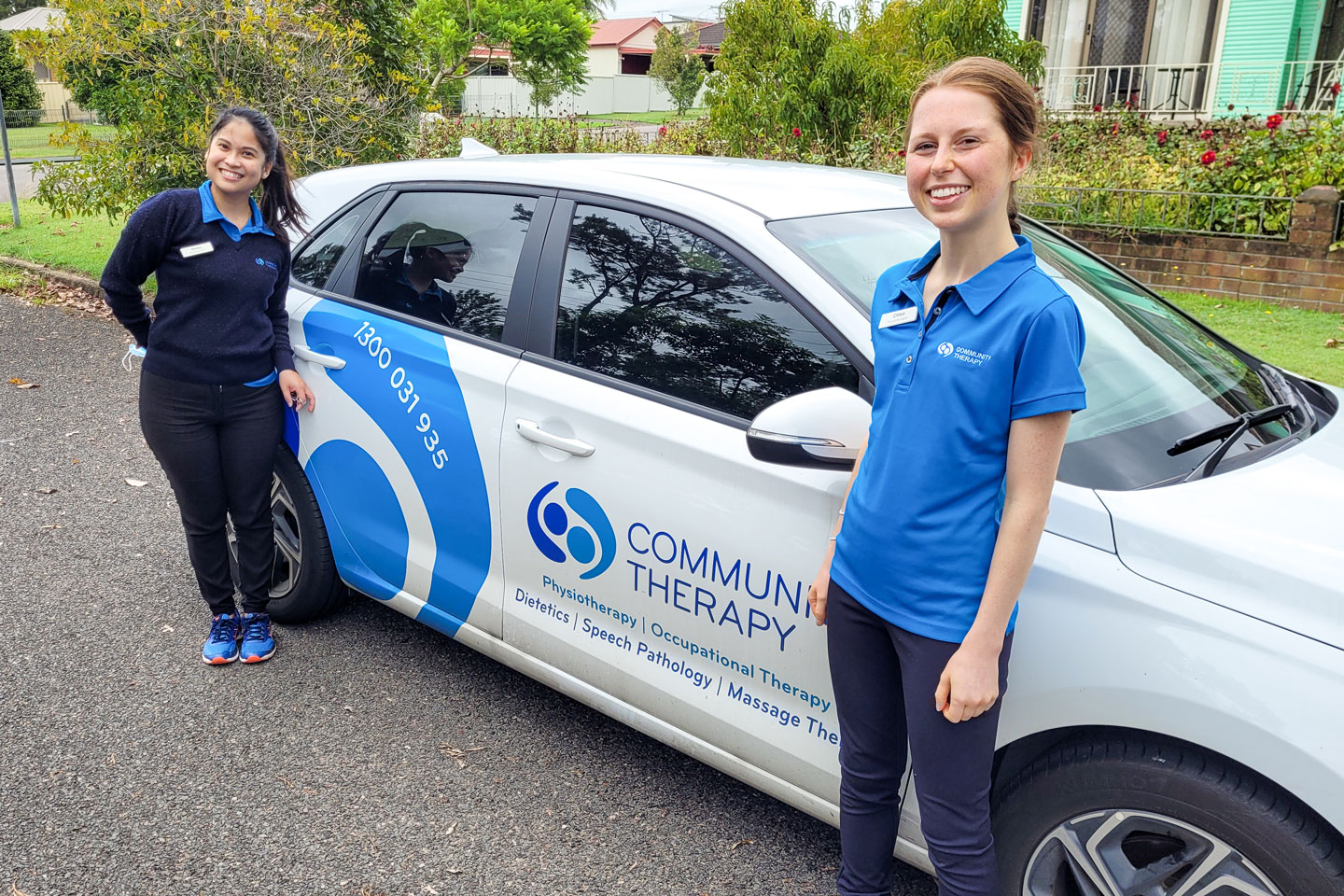 Two young clinicians smiling and standing next to a Community Therapy branded car