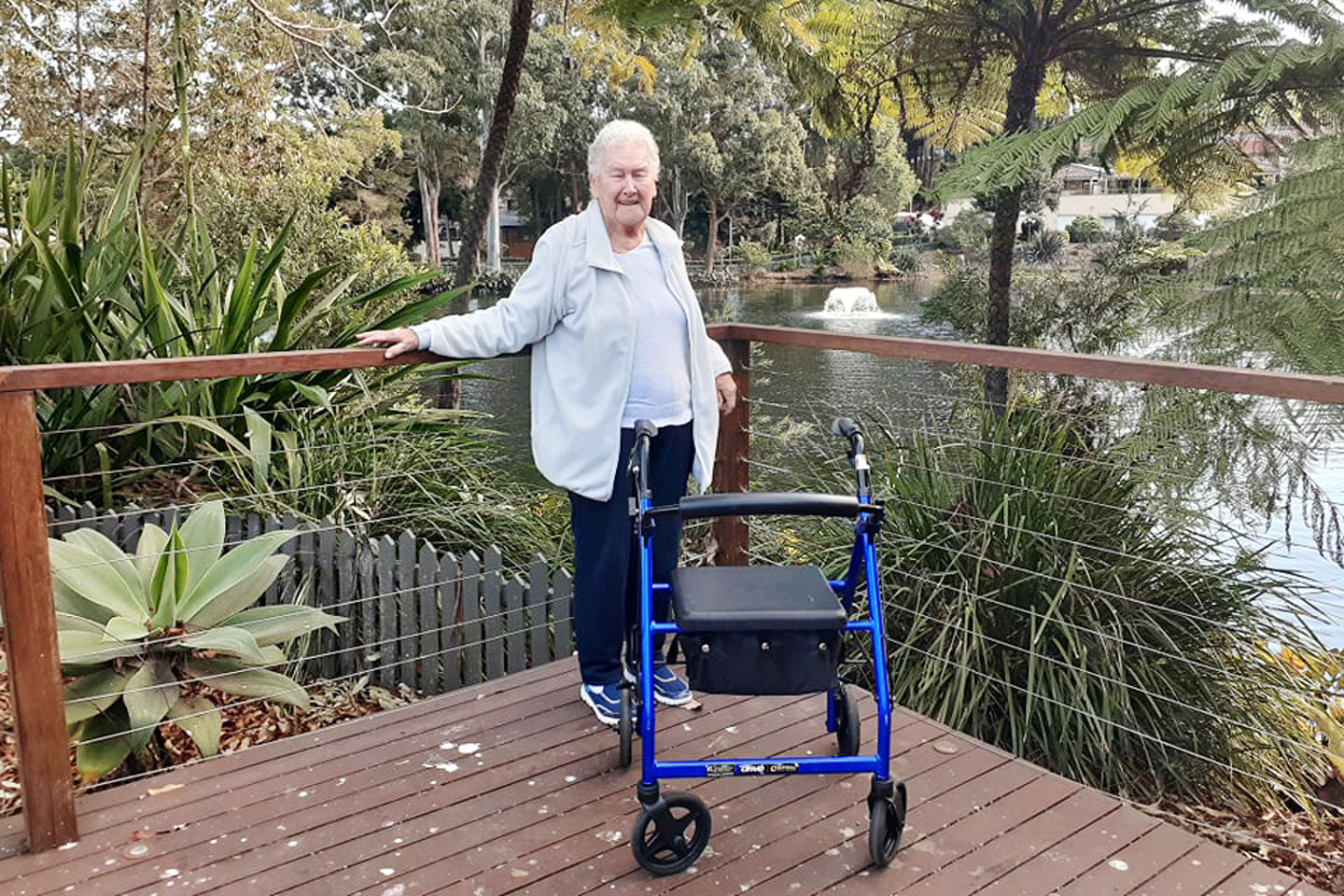 Older woman standing with her 4 wheel walker on a timber verandah and a nice view