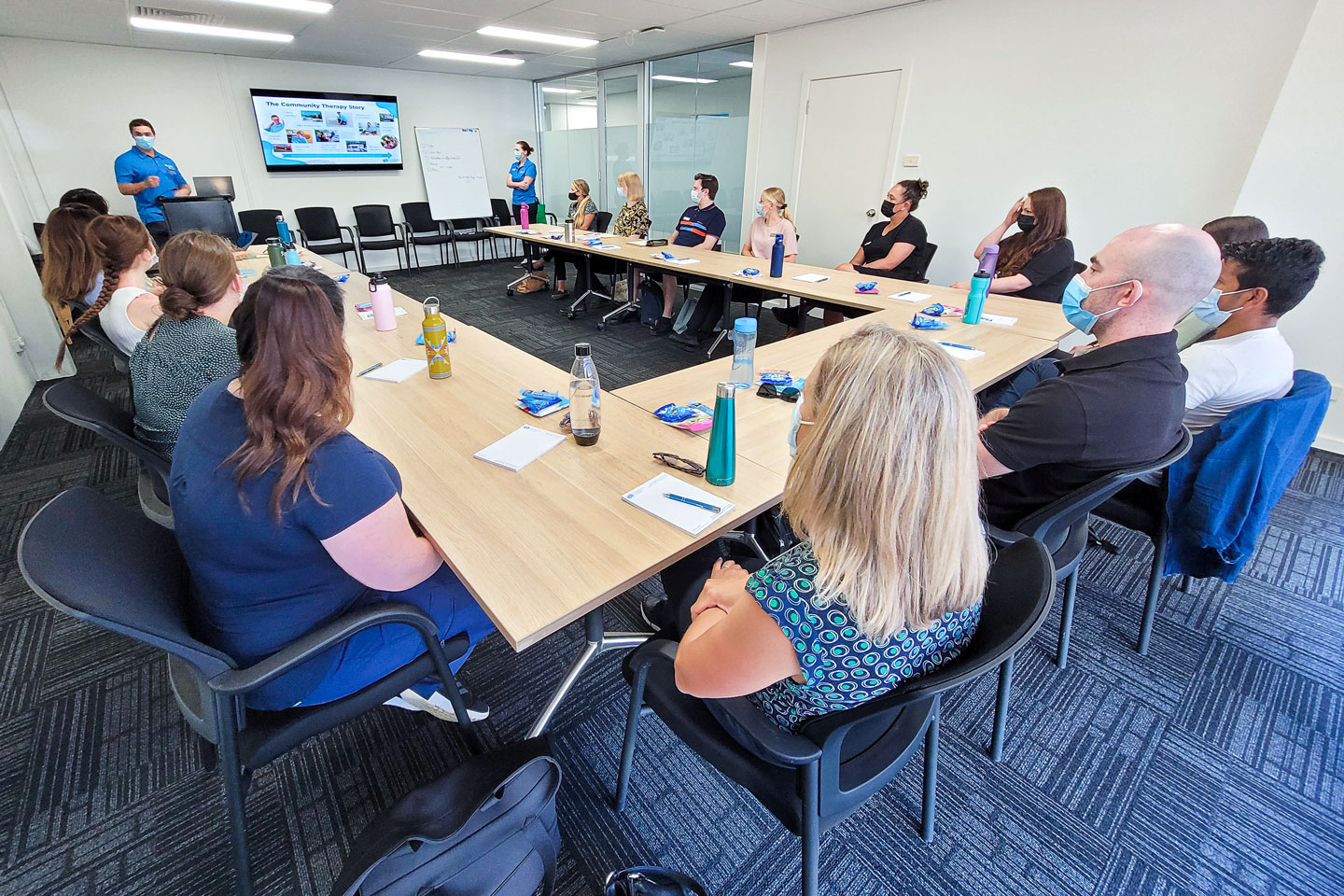 Group of people in the boarding room at Community Therapy headquarters looking at a presentation on the TV while a clinician speaks to the group
