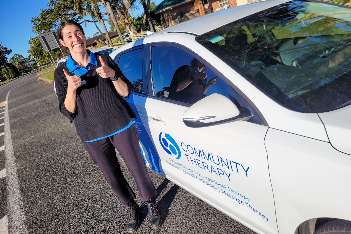 Clinician standing next to a branded Community Therapy car and showing both thumbs up