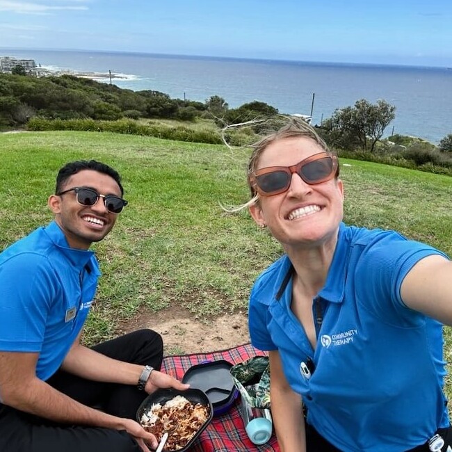 Mentor Bronte sitting on a grassy hill overlooking the beach with her buddy Pratik