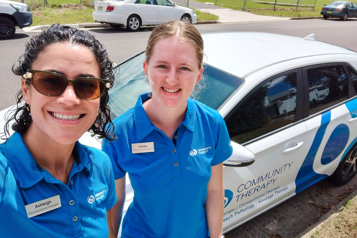 Selfie of two female Occupational Therapists smiling with a CT car in the background