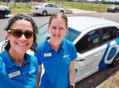 Two clinicians smiling in front of a branded car